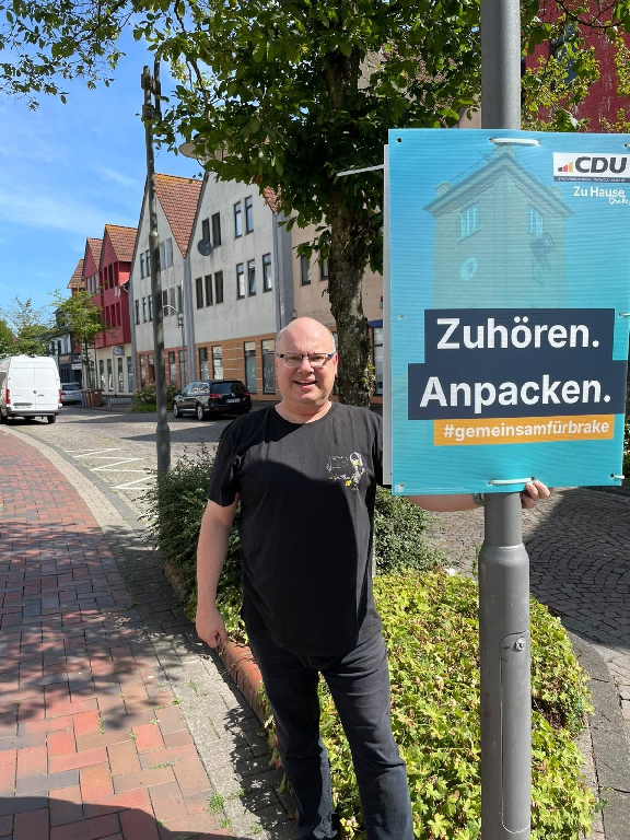 Claus Plachetka hängt ein CDU Plakat in Brake auf